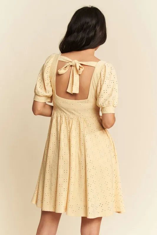 Back view of a romantic eyelet baby doll dress with puff sleeves and a bow detail in soft yellow