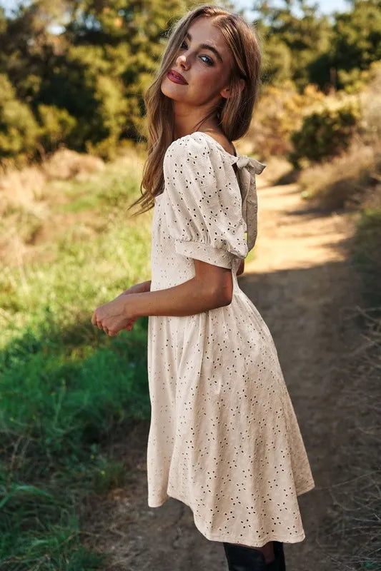 Chic female model wearing a romantic eyelet baby doll dress with a bow detail on the back outdoors
